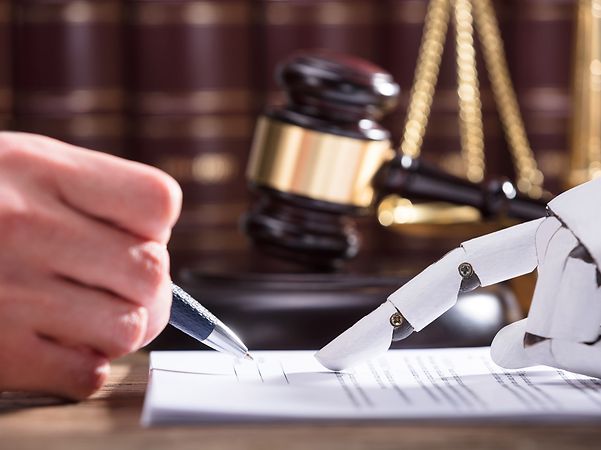 Hand und Roboterhand unterzeichnen ein Dokument, mit Richterhammer und Gesetzbüchern im Hintergrund