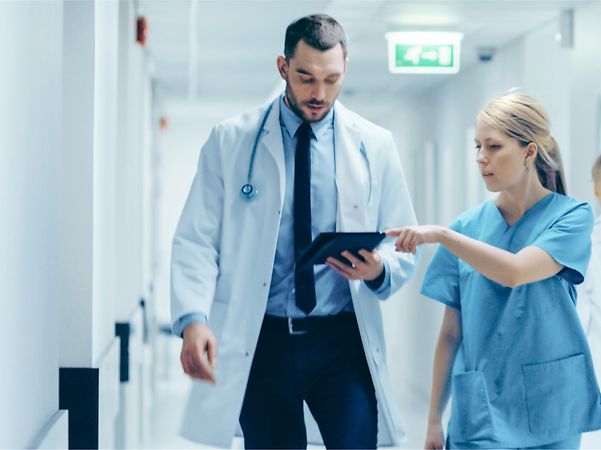 Arzt und Pflegekraft besprechen gemeinsam Informationen auf einem Tablet im Krankenhausflur.