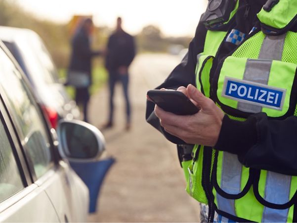 Polizeibeamter nutzt ein Smartphone bei einer Verkehrskontrolle am Straßenrand.