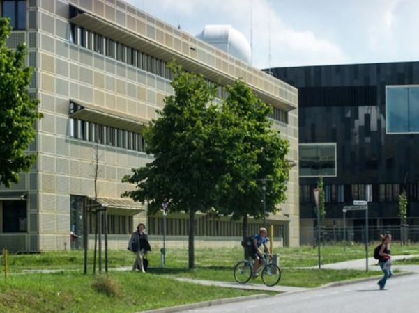 Moderne Hochschulgebäude der Universität Potsdam mit Grünfläche, Bäumen und vorbeifahrenden Radfahrern.