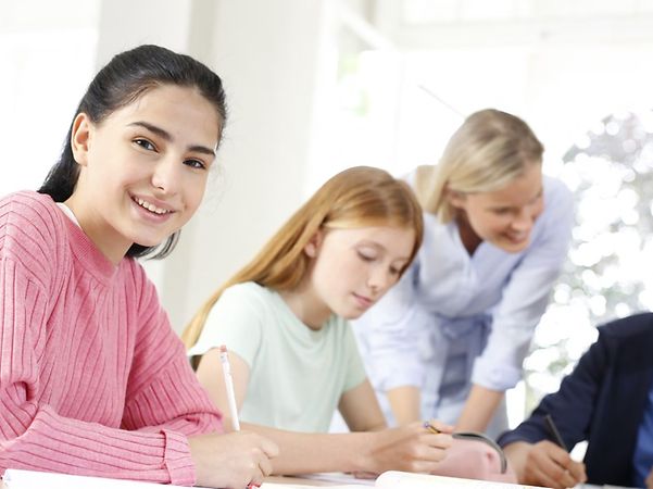 Schülerinnen und Schüler arbeiten gemeinsam mit einer Lehrkraft an einem Tisch.