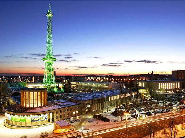 Beleuchtetes Messegelände Berlin mit Funkturm und Gebäuden bei Abenddämmerung.