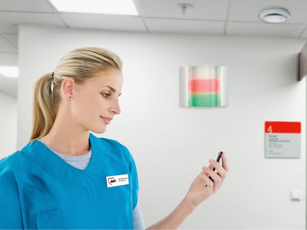 Pflegekraft im Krankenhaus betrachtet ein mobiles Gerät auf dem Flur.