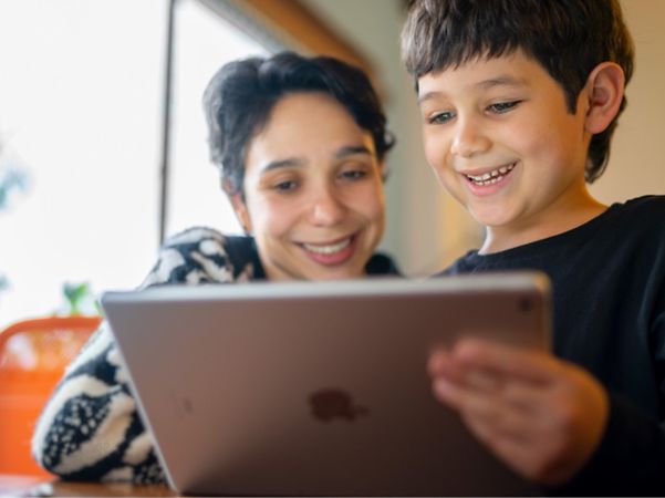 Zwei Kinder schauen gemeinsam lächelnd auf ein Tablet.