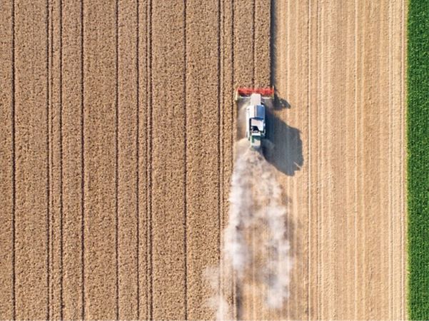 Luftaufnahme eines Traktors, der auf einem Feld arbeitet und Staub aufwirbelt.