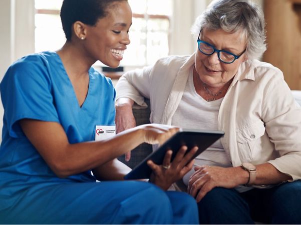 Pflegekraft zeigt einer älteren Frau lächelnd Inhalte auf einem Tablet.