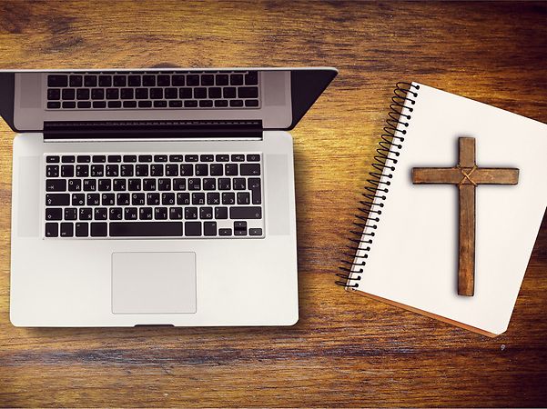 Laptop neben Notizbuch mit Kreuz symbolisiert die Digitalisierung der Kirche.