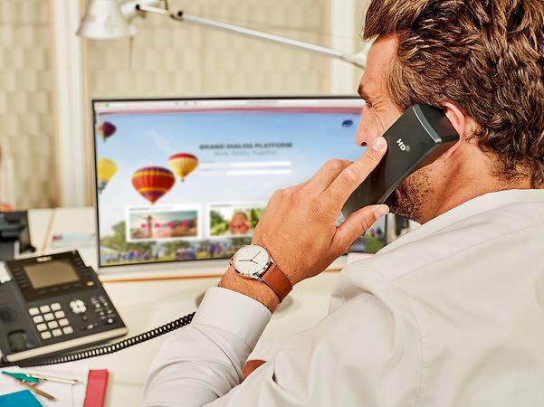 Person telefoniert im Büro am Festnetz vor einem Bildschirm mit Präsentation