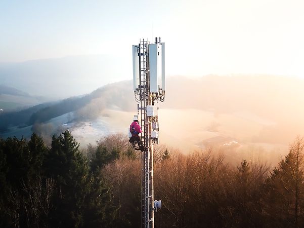 Fachkraft arbeitet auf einem Mobilfunkturm in einer bewaldeten Hügellandschaft