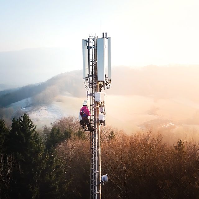 Fachkraft arbeitet an einem Mobilfunkturm in einer hügeligen Landschaft