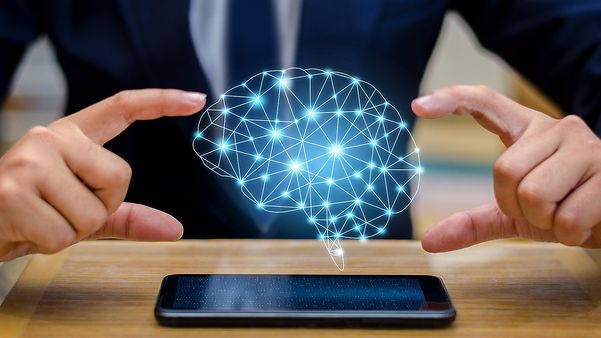 Person an Endgerät, über dem schwebt abstrakte Projektion eines Gehirns, das für fachliche/ technische Transformation steht.
