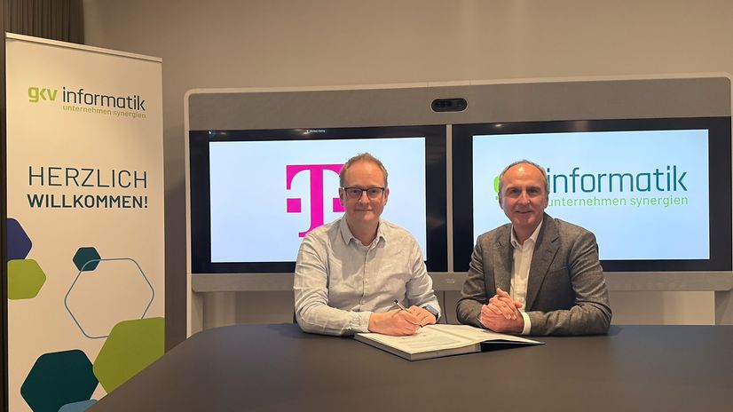 Zwei Männer sitzen vor gkv-informatik- und Telekom-Displays.