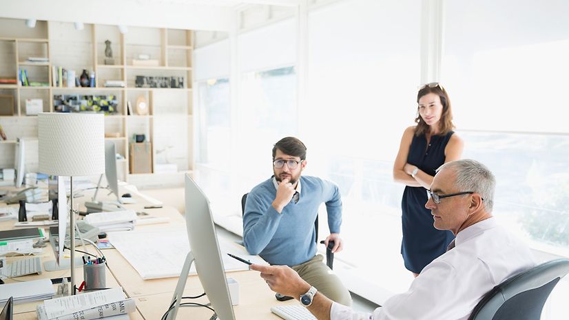 Drei Personen besprechen sich in einem hellen Büro an einem Computer.