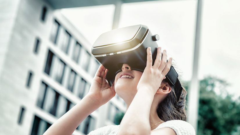 Schülerin trägt eine VR-Brille vor einem unscharfen Schulgebäude.