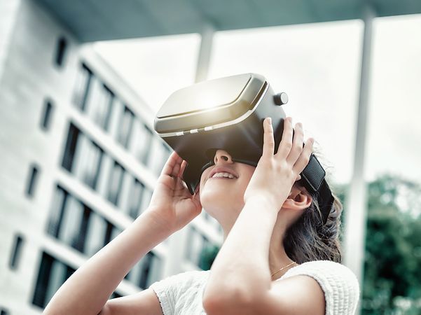 Schülerin trägt eine VR-Brille vor einem unscharfen Schulgebäude.