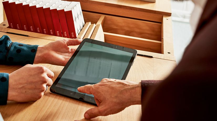 Zwei Personen bedienen gemeinsam ein Tablet auf einem Holztisch.