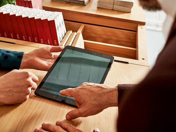 Zwei Personen bedienen gemeinsam ein Tablet auf einem Holztisch.