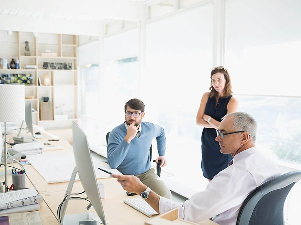 Drei Personen arbeiten zusammen im Büro und besprechen Inhalte auf einem Monitor.