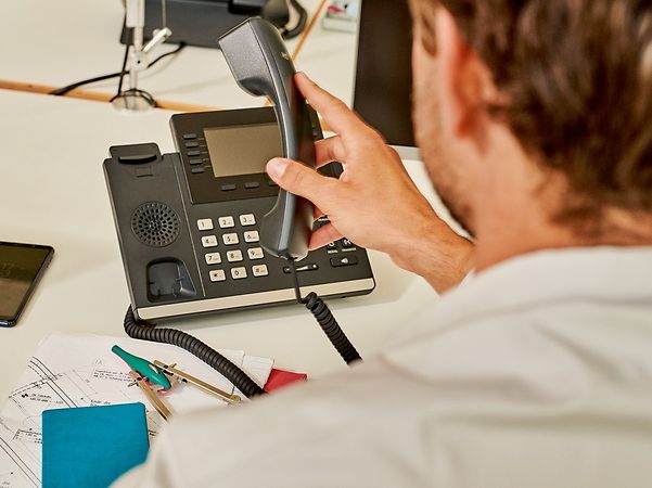 Person bedient ein Festnetztelefon am Schreibtisch.