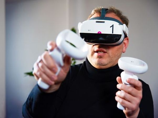 Person nutzt eine Virtual-Reality-Brille und hält zwei Controller in den Händen.