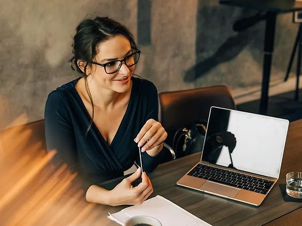 Frau sitzt an einem Tisch mit Laptop und Stift.