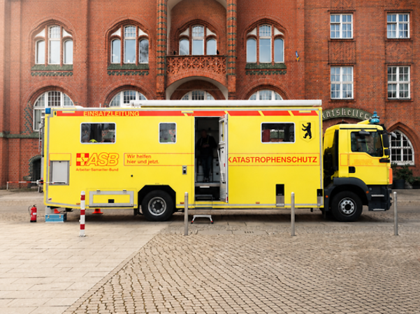 Vier Personen stehen in Arbeitskleidung in einem Gewächshaus und halten ein Schild mit der Aufschrift „Das Zusammen wirkt.“